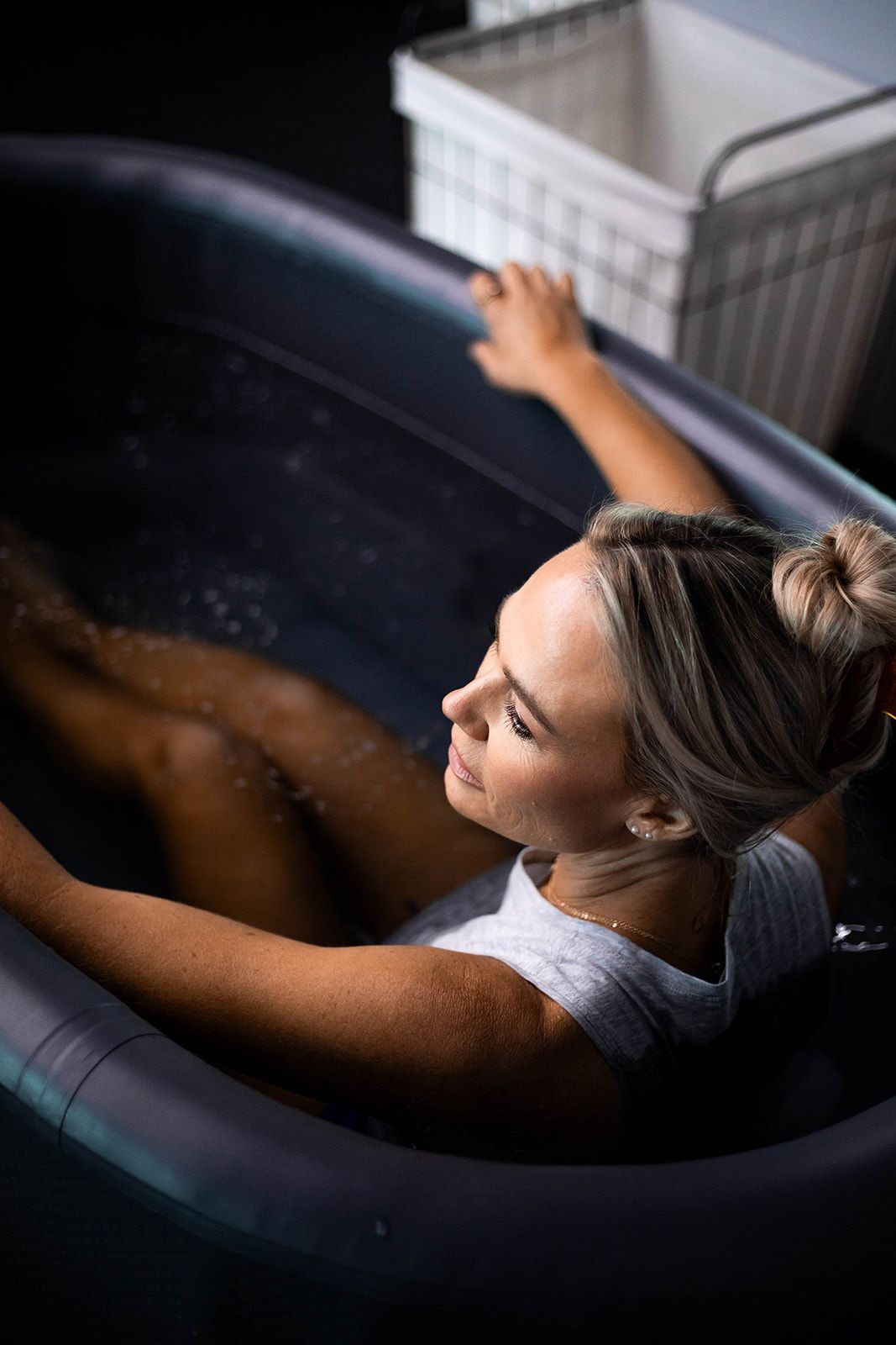 Woman relaxing in an inflatable tub filled with water, with a wire basket in the background.