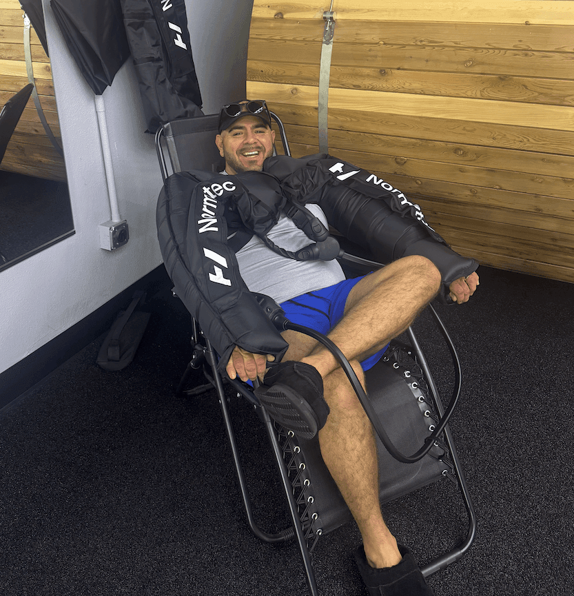 Man smiling while using compression therapy sleeves on arms and legs in a relaxation chair.