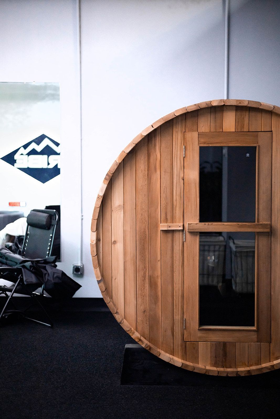 Wooden barrel-shaped sauna in a room with a chair and mirror nearby.